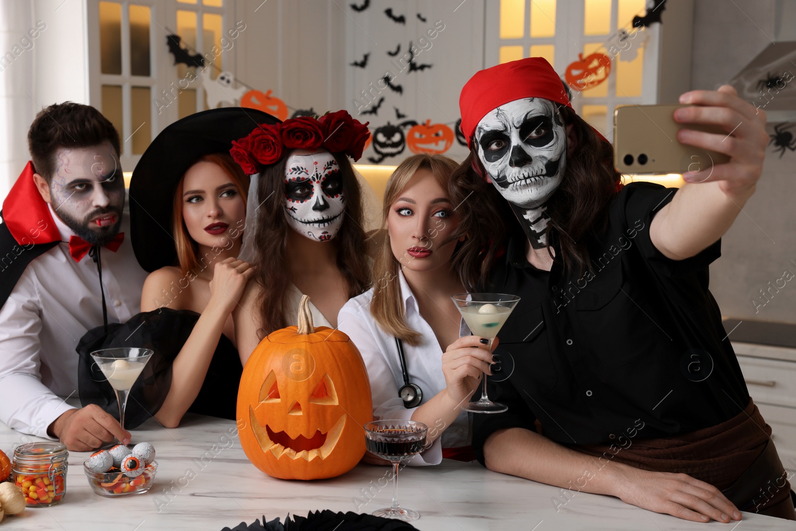 Photo of Group of people in scary costumes with cocktails taking selfie at Halloween party indoors