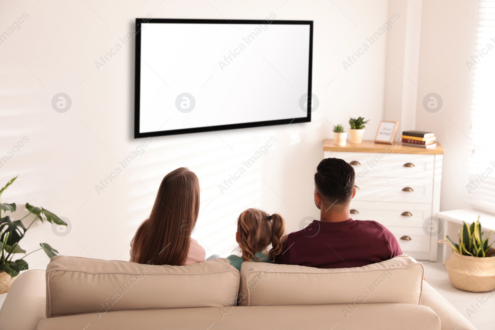 Photo of Family watching TV on sofa at home, back view