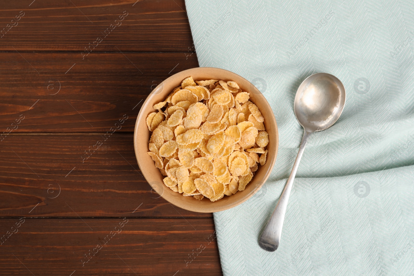 Photo of Bowl with healthy cornflakes and spoon on wooden table, top view