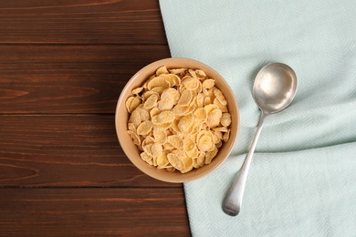 Photo of Bowl with healthy cornflakes and spoon on wooden table, top view