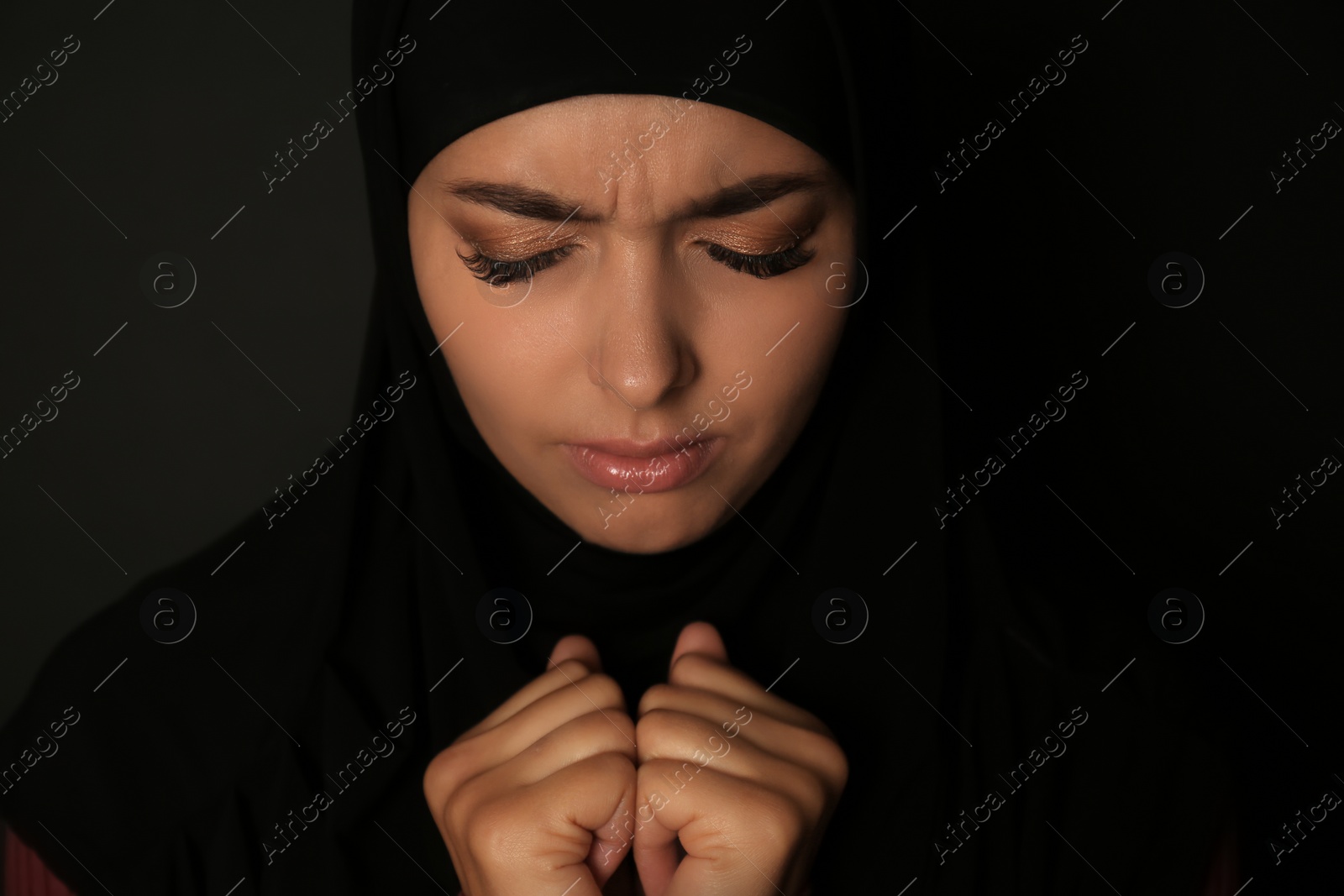 Photo of Portrait of sad Muslim woman in hijab  praying on dark background