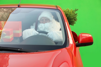 Authentic Santa Claus with fir tree and presents driving car against green background