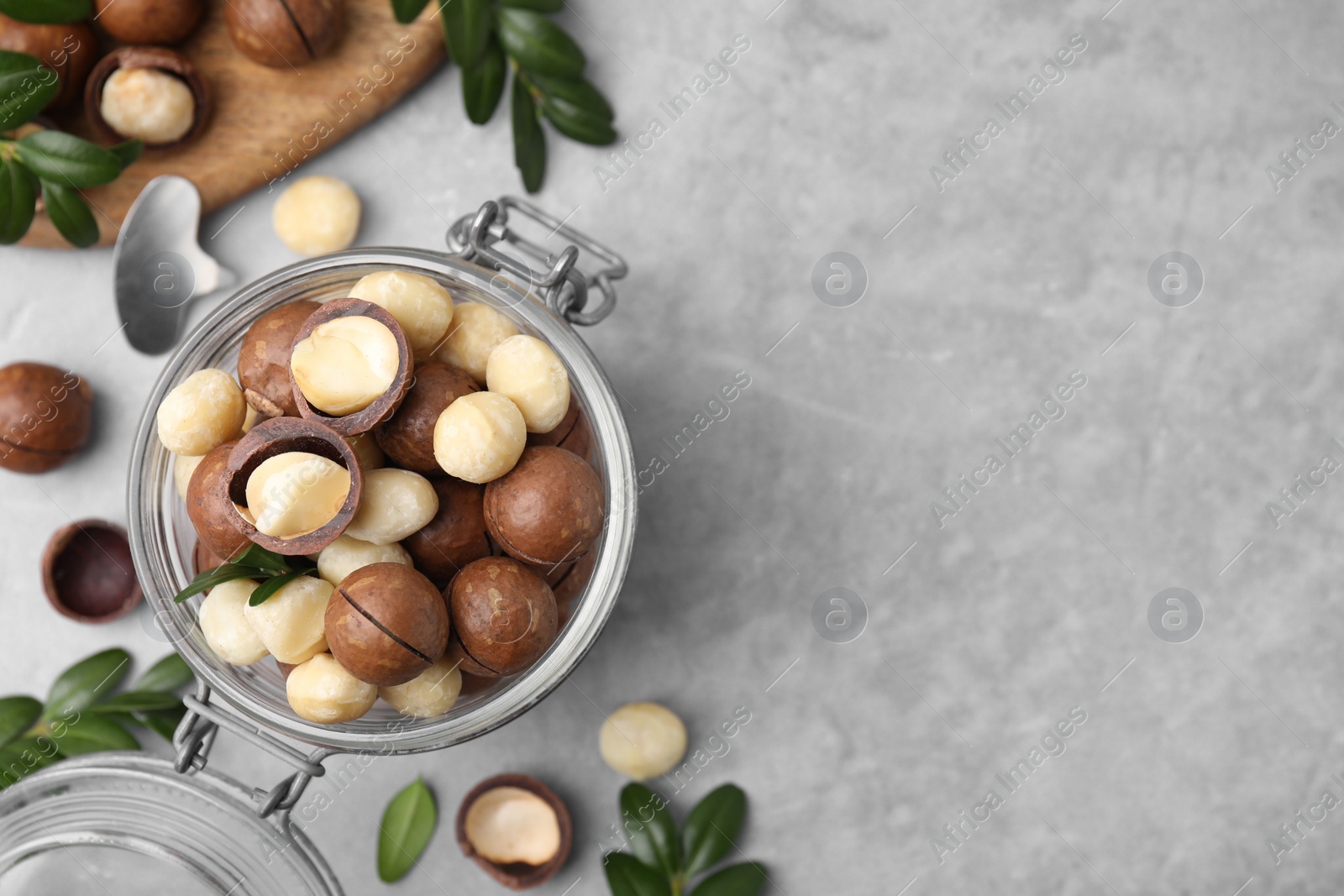 Photo of Tasty Macadamia nuts in jar on light grey table, flat lay. Space for text