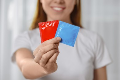 Photo of Woman holding condoms indoors, closeup. Safe sex