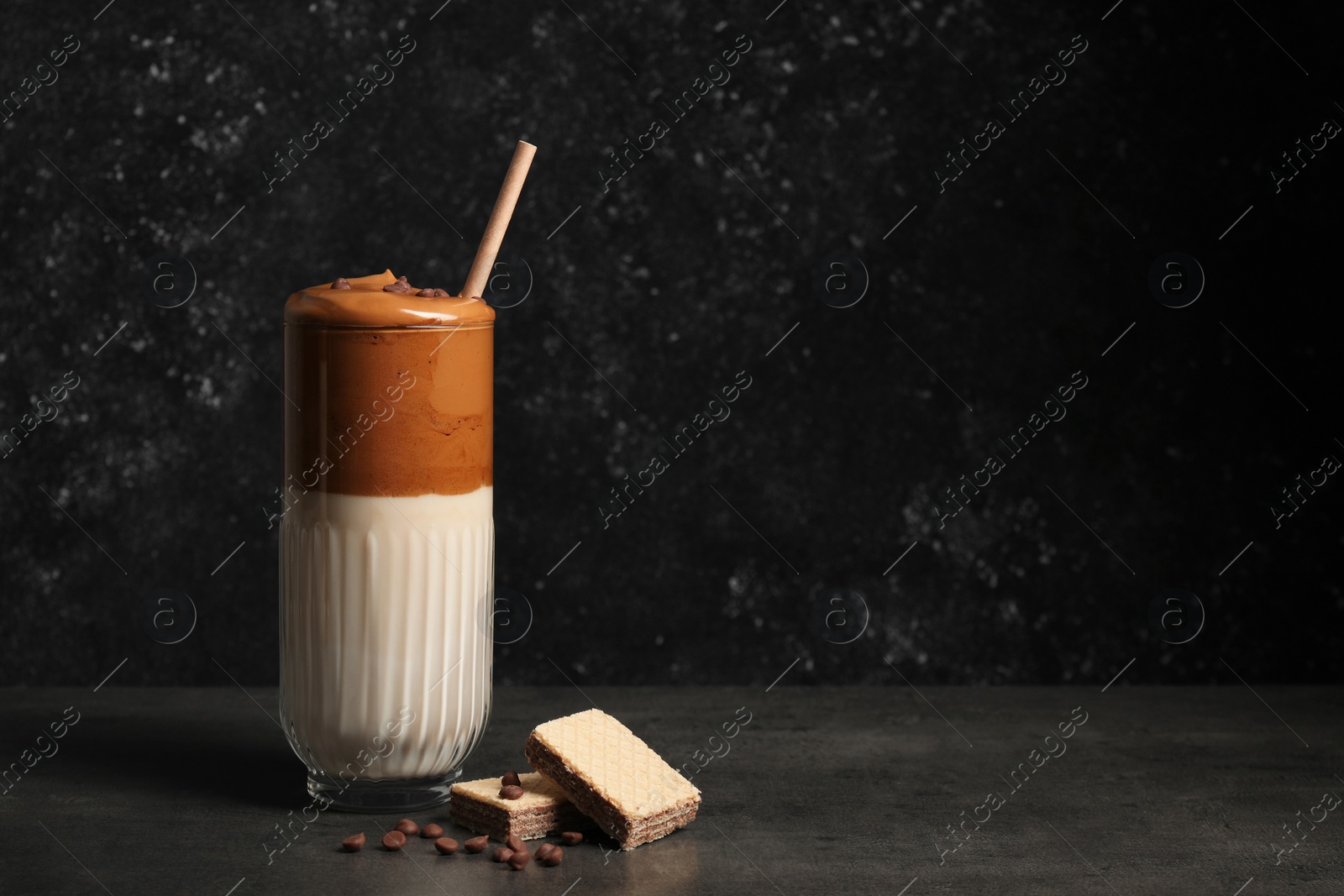 Photo of Glass of delicious dalgona coffee with chocolate chips and waffles on dark table, space for text