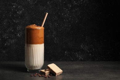 Photo of Glass of delicious dalgona coffee with chocolate chips and waffles on dark table, space for text