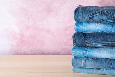 Stack of different jeans on wooden table against pink background. Space for text