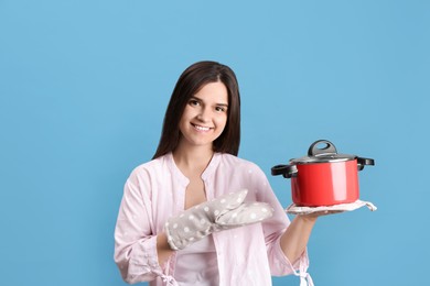 Photo of Happy young woman with cooking pot on light blue background