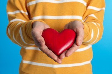 Woman holding decorative heart on color background, closeup