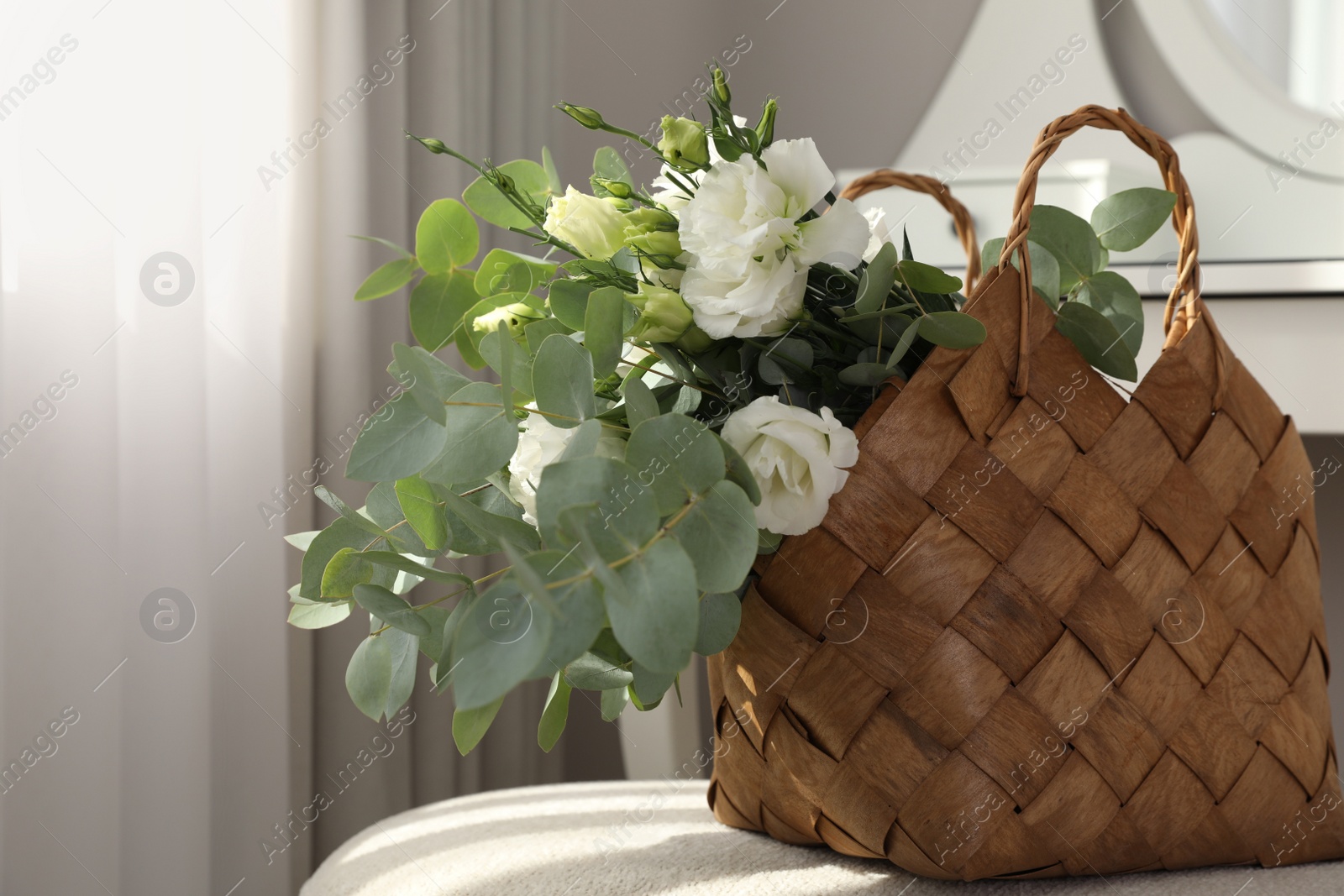 Photo of Stylish wicker basket with bouquet of flowers on ottoman in room