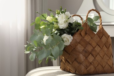 Stylish wicker basket with bouquet of flowers on ottoman in room