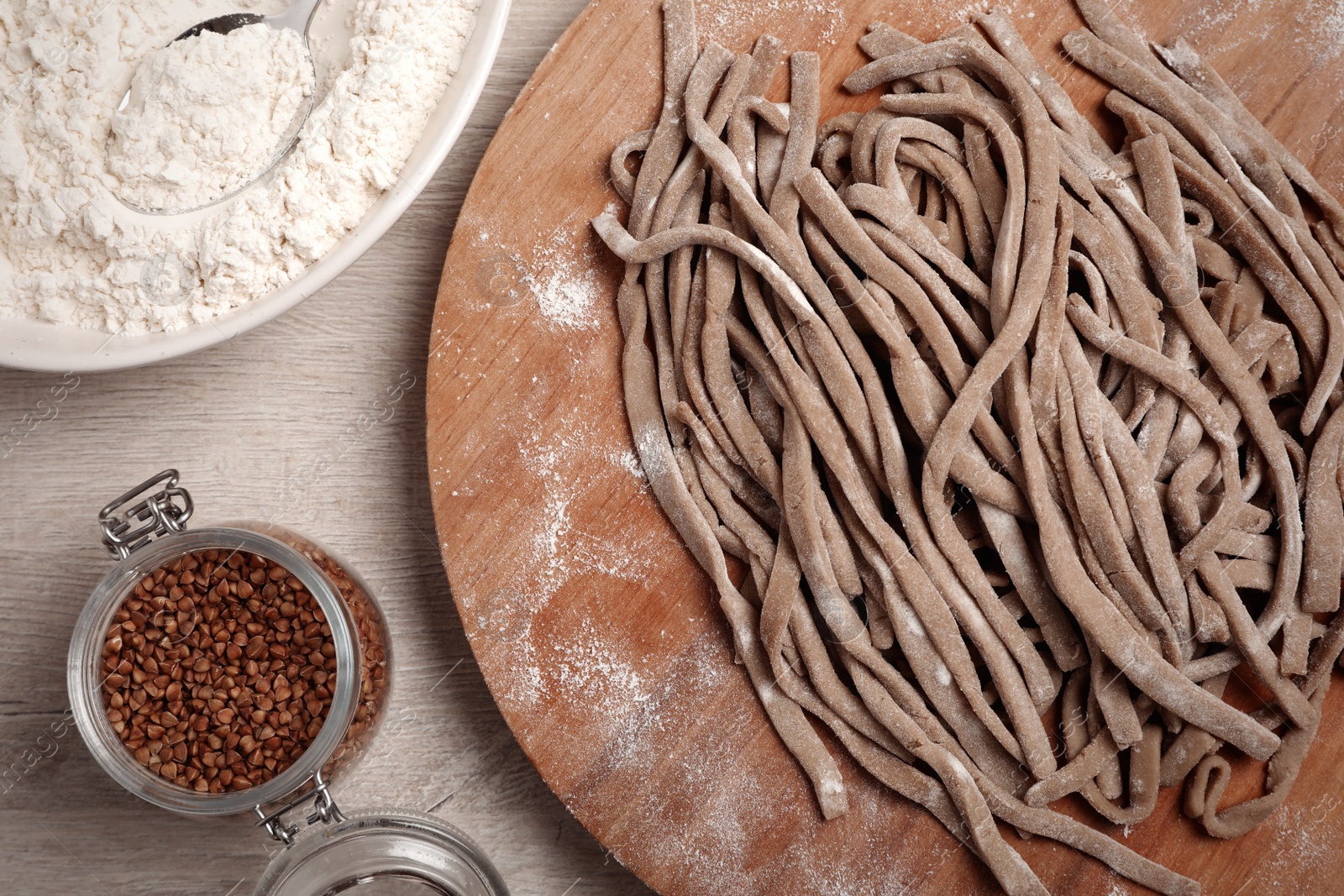 Photo of Uncooked homemade soba (buckwheat noodles), flour and grains on wooden table, flat lay