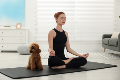 Young woman practicing yoga on mat with her cute dog at home