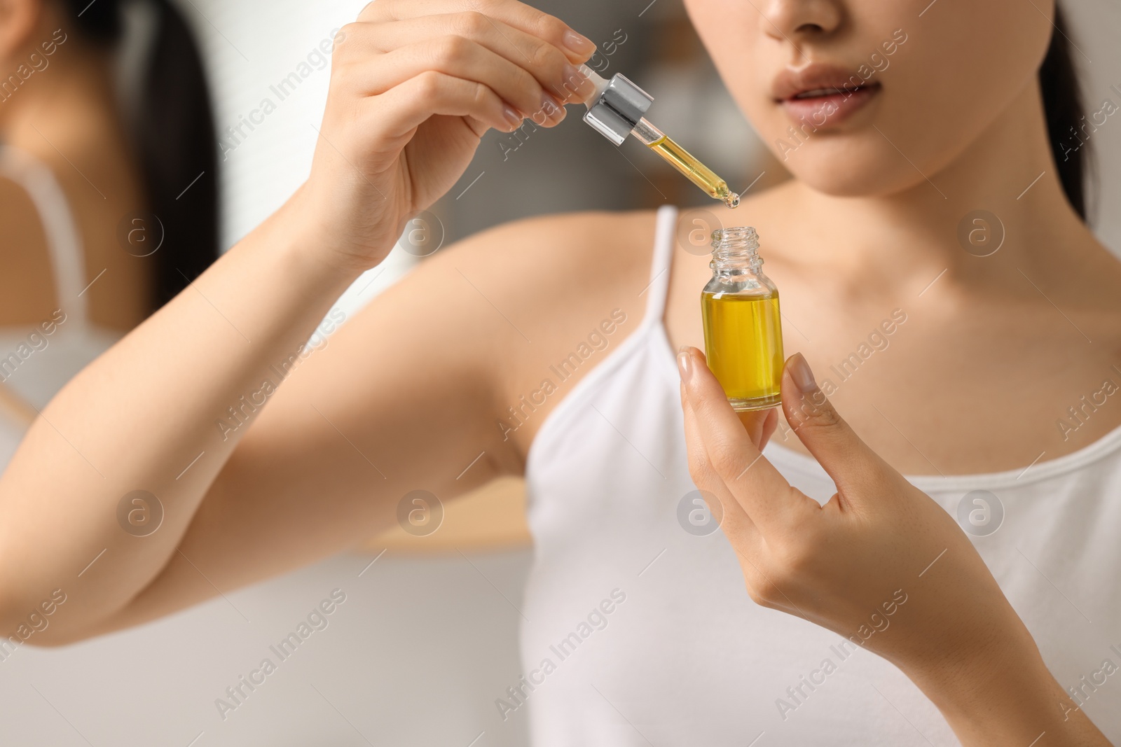 Photo of Beautiful young woman with bottle of cosmetic serum in bathroom, closeup