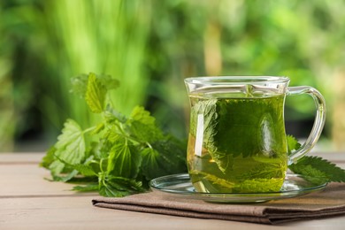 Photo of Glass cup of aromatic nettle tea and green leaves on wooden table outdoors, space for text