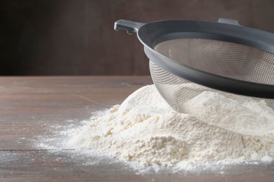 Photo of Sieve and pile of flour on wooden table, closeup. Space for text