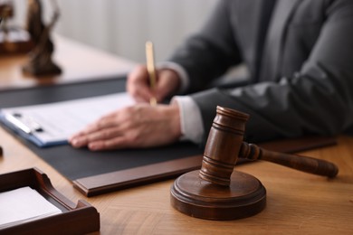 Notary writing notes at wooden table in office, focus on gavel