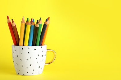 Photo of Colorful pencils in cup on yellow background. Space for text