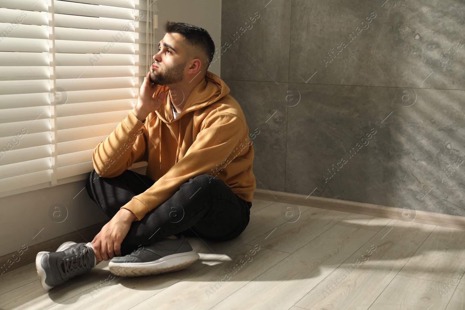 Photo of Sad man sitting on floor near window. Space for text