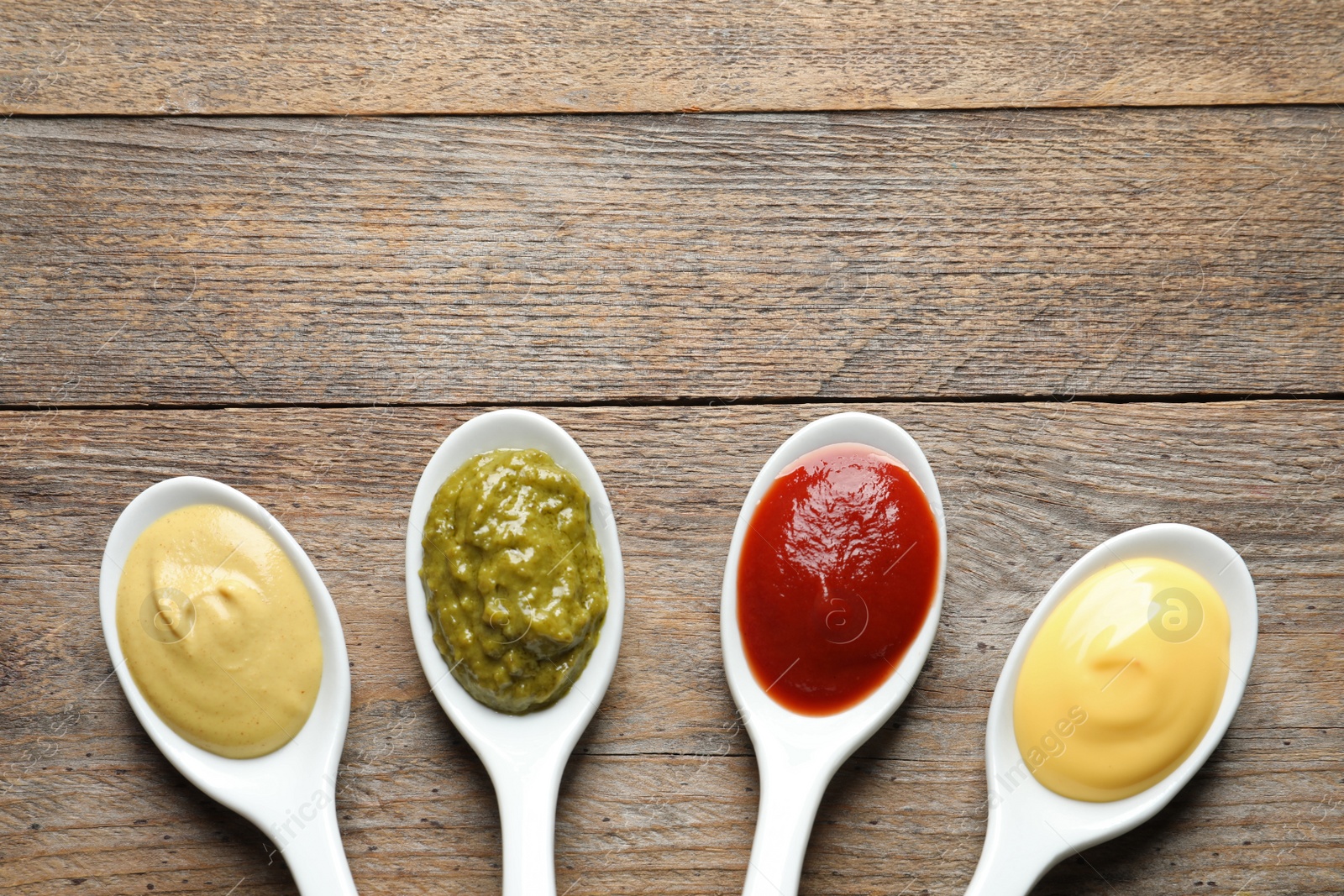 Photo of Spoons with different sauces and space for text on wooden background, flat lay