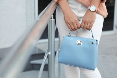 Young woman with stylish light blue bag near railing outdoors, closeup