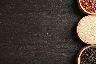 Photo of Flat lay composition with brown and other types of rice in bowls on wooden background. Space for text