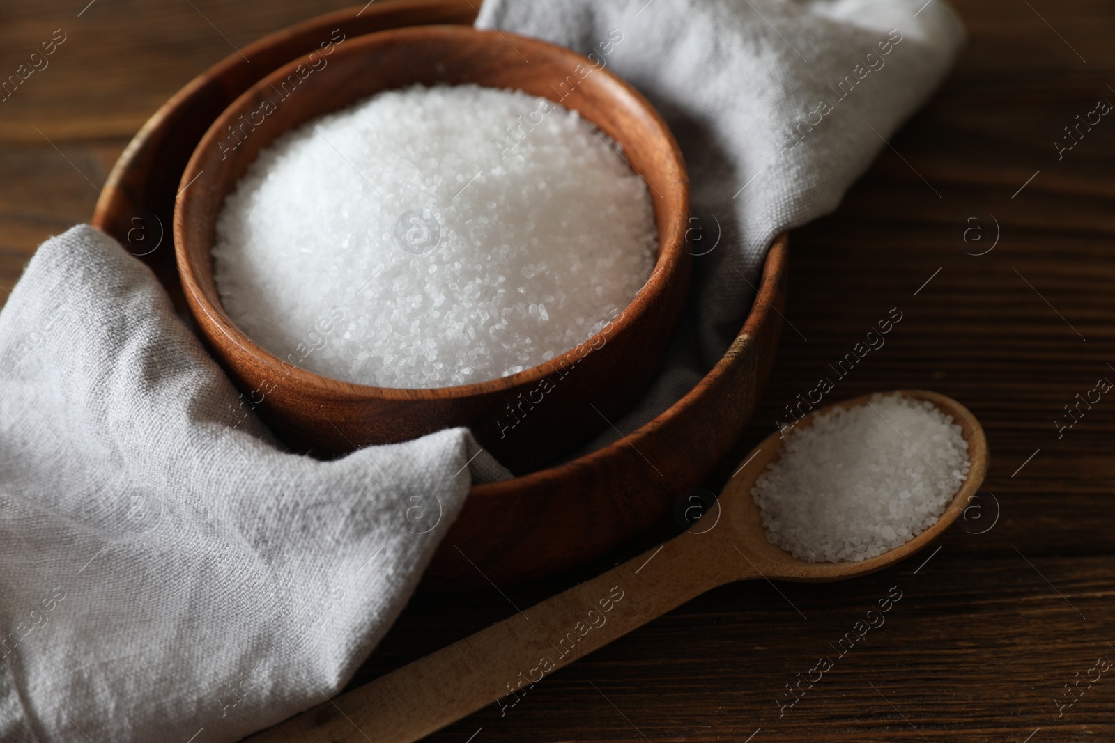 Photo of Organic salt in bowl and spoon on wooden table, closeup