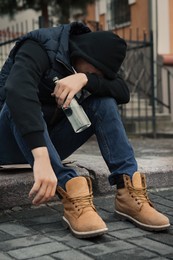 Addicted drunk man with alcoholic drink on stairs outdoors