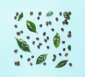 Fresh green coffee leaves and beans on light blue background, flat lay