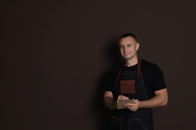 Photo of Portrait of happy young waiter with notebook on brown background, space for text