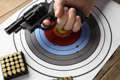 Photo of Man with handgun near shooting target and bullets at table, closeup