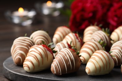 Photo of Delicious chocolate covered strawberries, flowers and burning candles on table, closeup