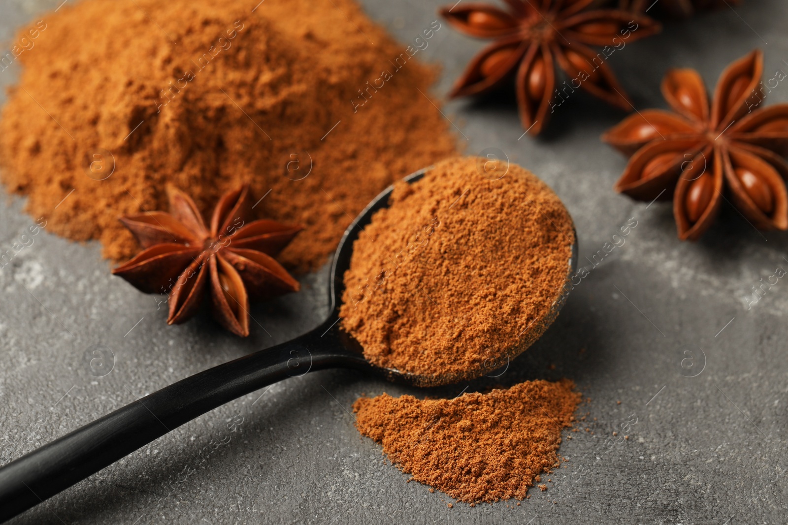 Photo of Spoon with cinnamon powder and star anise on grey table, closeup