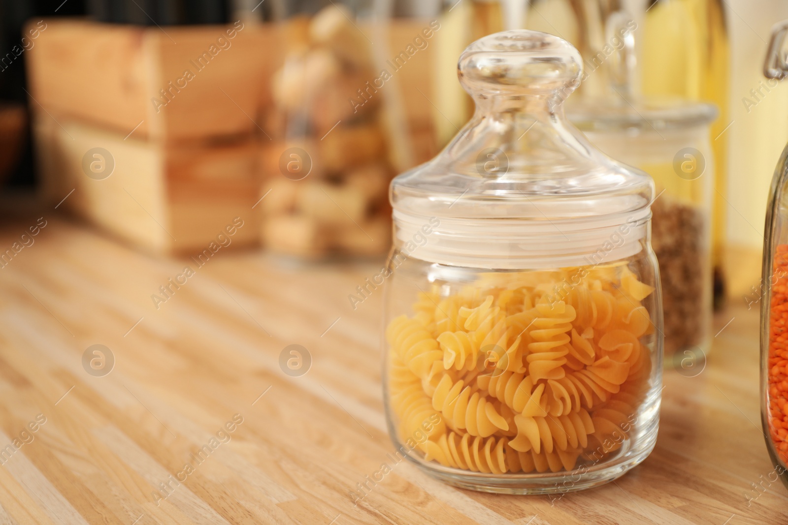 Photo of Glass jar with pasta on wooden countertop in kitchen, space for text