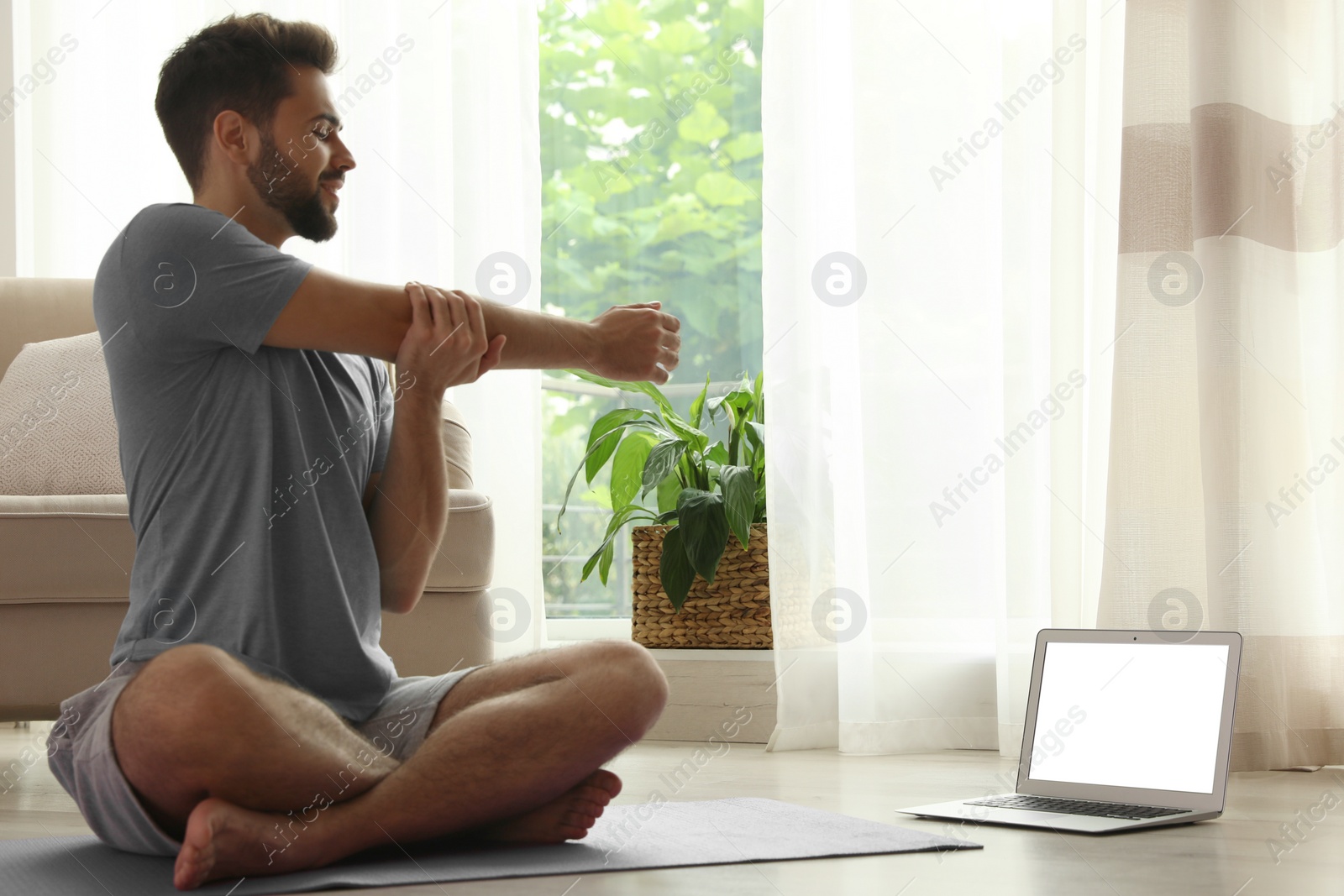 Photo of Man practicing yoga while watching online class at home during coronavirus pandemic. Social distancing