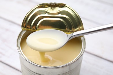 Taking tasty condensed milk from tin can with spoon at white table, closeup