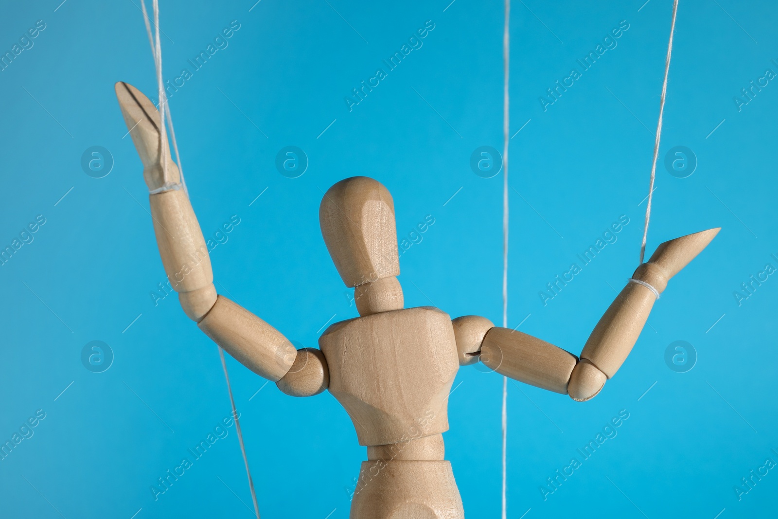 Photo of One wooden puppet with strings on light blue background