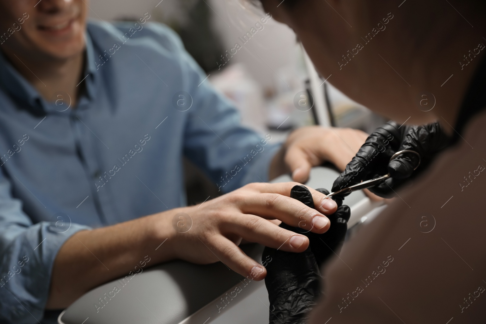 Photo of Professional manicurist cutting client's cuticle in beauty salon, closeup