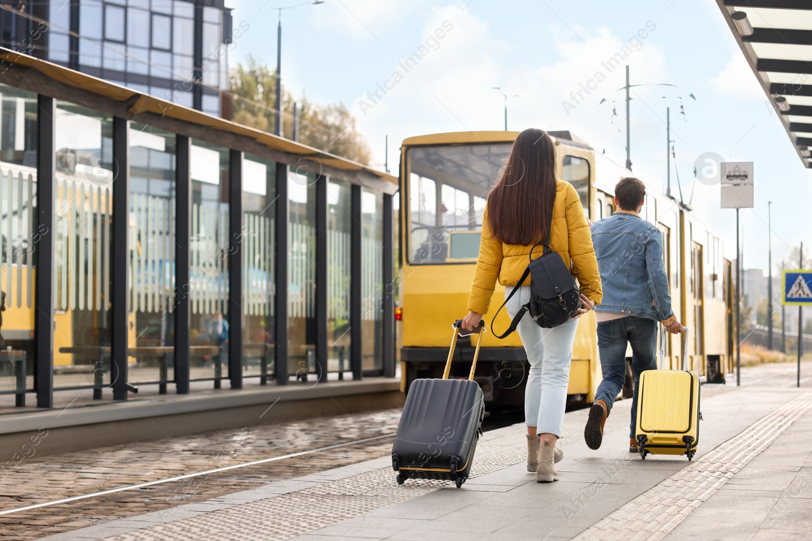 Photo of Being late. Couple with suitcases walking towards tram outdoors, back view. Space for text