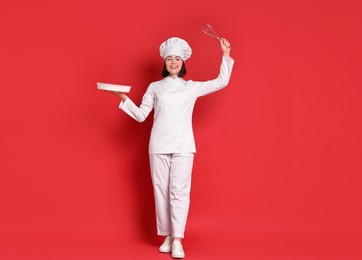 Photo of Happy confectioner holding whisk and baking dish on red background