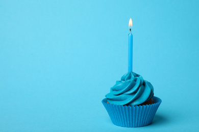 Photo of Delicious birthday cupcake with burning candle on light blue background. Space for text