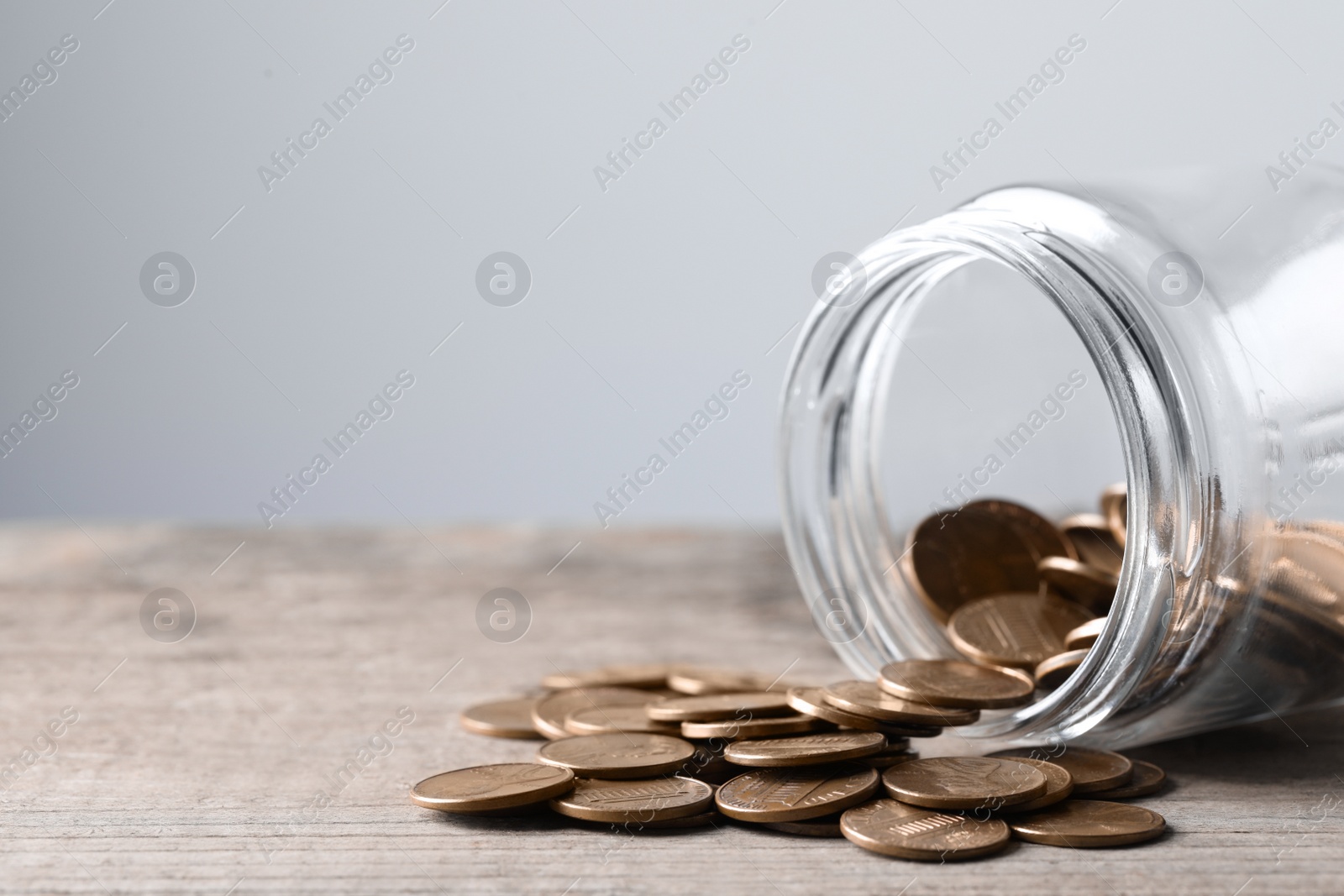 Photo of Glass jar with coins on wooden table, closeup. Space for text