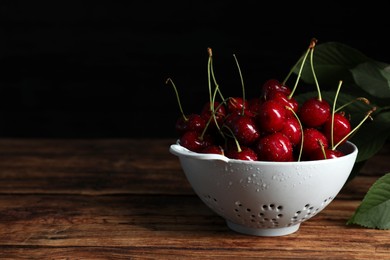 Wet red cherries in colander on wooden table, space for text