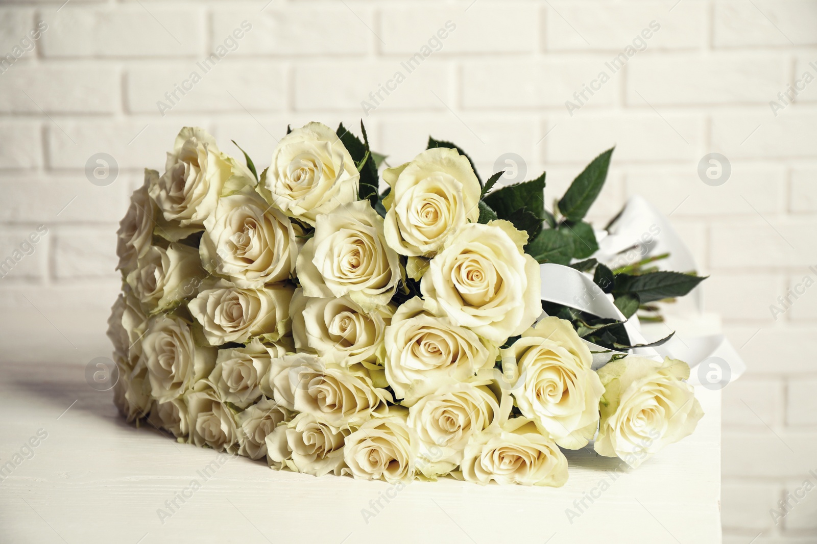 Photo of Luxury bouquet of fresh roses on table near white brick wall