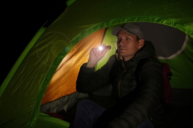 Man with flashlight sitting in tent at night