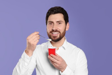 Photo of Handsome man with delicious yogurt and spoon on violet background
