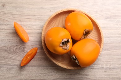 Photo of Delicious ripe persimmons on light wooden table, top view