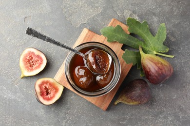 Photo of Jar of tasty sweet jam, fresh figs and green leaf on grey table, flat lay