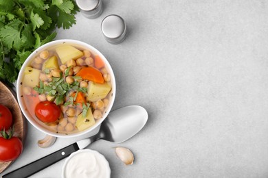 Photo of Flat lay composition of tasty chickpea soup in bowl, vegetables, sauce and spices served on light grey table. Space for text