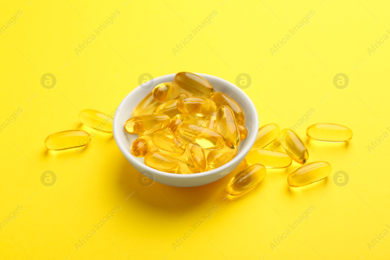 Photo of Vitamin capsules in bowl on yellow background